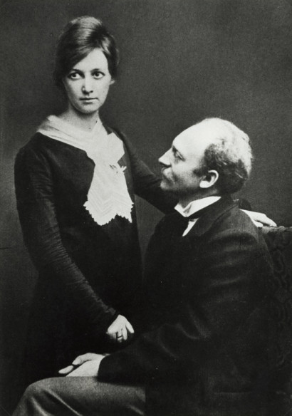 Ada Nolde steht in schwarzem Kleid mit wei&szlig;em Tuch, Emil Nolde sitzt auf einem Stuhl in schwarzem Anzug und blickt zu ihr.