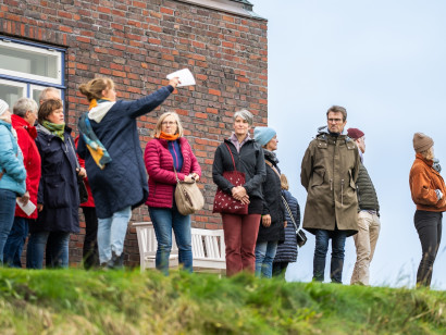 Gef&uuml;hrte Besuchergruppe in Herbstkleidung vor dem Nolde-Haus, die aufmerksam in Richtung Nolde-Garten und Botanicum blickt.