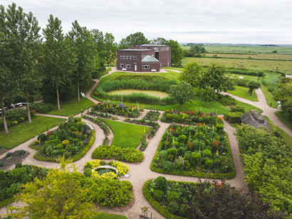 Luftaufnahme des Nolde-Hauses mit gr&uuml;nem Garten und weiter Marschlandschaft an einem hellen, bew&ouml;lkten Tag im sp&auml;ten Fr&uuml;hling.